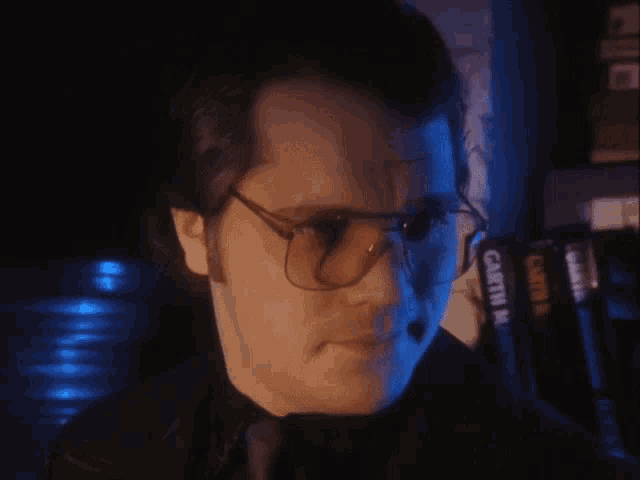 a man wearing glasses and a black shirt is standing in front of a row of casette m books