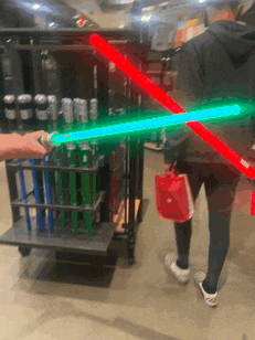 a person is holding a green light saber in front of a cart full of cans