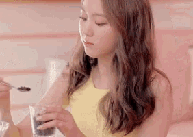 a woman in a yellow tank top is holding a glass and a spoon