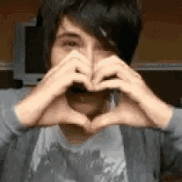 a young man is making a heart shape with his hands .