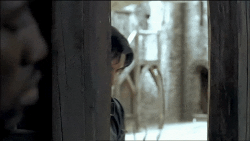 a man looking through a wooden door with another man behind him