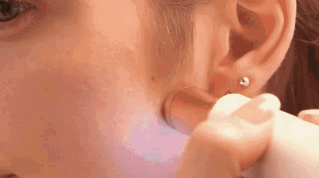 a close up of a woman 's ear with a purple light shining on it