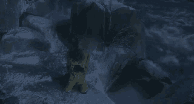 a person in shorts is standing in the snow near a rock .