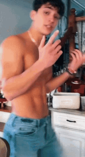 a shirtless man is standing in a kitchen with his hands up .