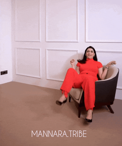 a woman in a red jumpsuit is sitting in a chair with the words mannara.tribe behind her