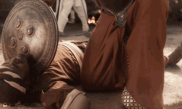 a man laying on the ground holding a shield with the words mandamurisans on the bottom right