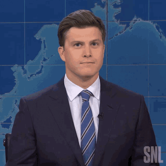 a man in a suit and tie stands in front of a snl map