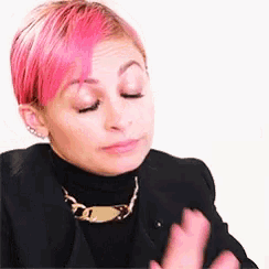 a woman with pink hair wearing a black jacket and a gold necklace