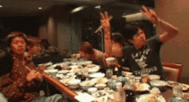 a group of people are sitting around a table with plates of food and a man wearing a t-shirt that says tokyo