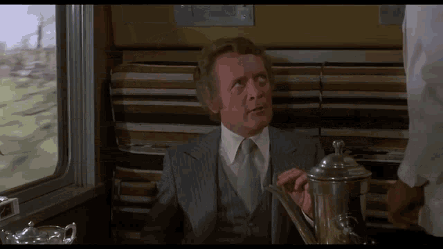 a man in a suit and tie is sitting on a couch with a teapot