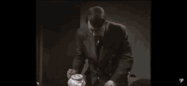 a man in a suit is pouring liquid into a jar .