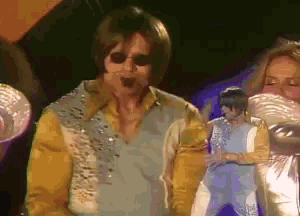 a man wearing sunglasses and a yellow shirt is dancing with two women