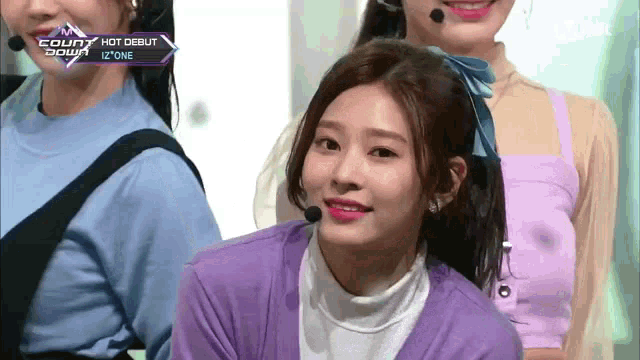 a girl in a purple sweater is smiling in front of a microphone with the words count down on the screen behind her