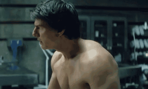 a shirtless man is standing in a dark room looking at something .