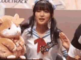 a girl in a sailor outfit is holding a stuffed animal and waving .