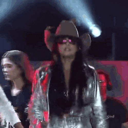 a woman is wearing a cowboy hat and sunglasses on a stage .