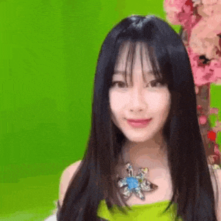 a woman with long black hair and a flower necklace is smiling in front of a green background .