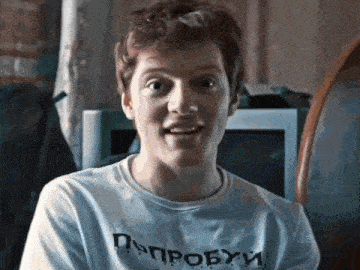 a young man wearing a t-shirt with russian writing on it is smiling .