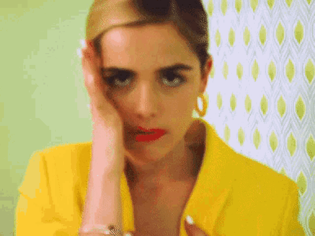 a woman wearing a yellow jacket and hoop earrings covering her face with her hand