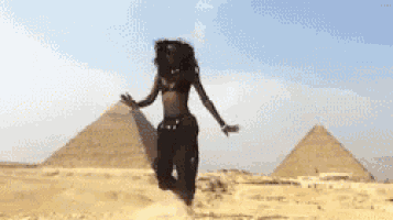 a woman is dancing in front of two pyramids in the desert .