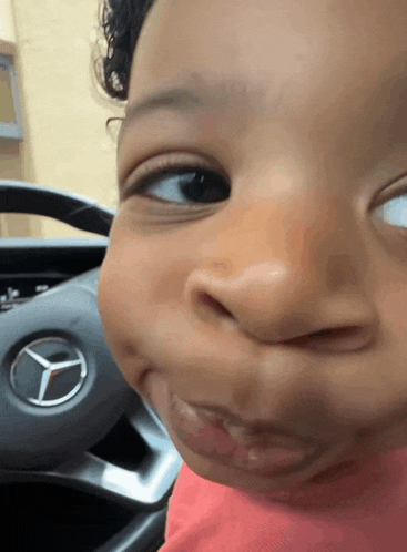 a baby is making a funny face in front of a mercedes steering wheel