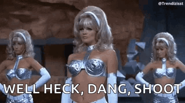 a woman in a silver bra and gloves is standing next to two other women in silver costumes .