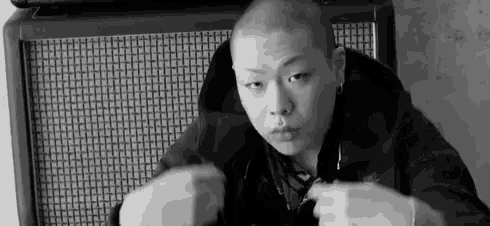 a black and white photo of a shaved headed man sitting in front of a speaker .
