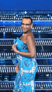 a man wearing glasses and a blue dress stands in front of a blue backdrop