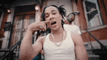 a young man wearing a white tank top and a gold chain is sitting on a set of stairs .