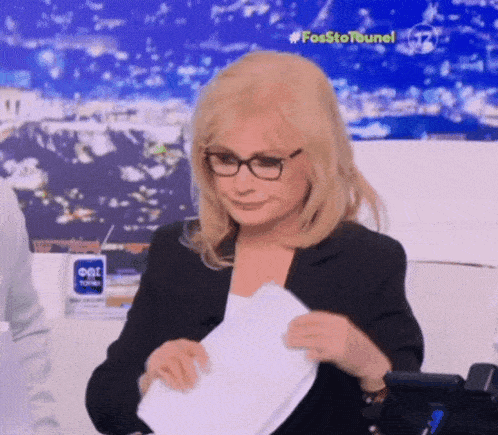 a woman wearing glasses holds a piece of paper in front of a sign that says fosstotourel