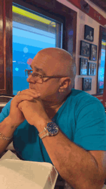 a man wearing glasses and a watch is sitting at a table in front of a window