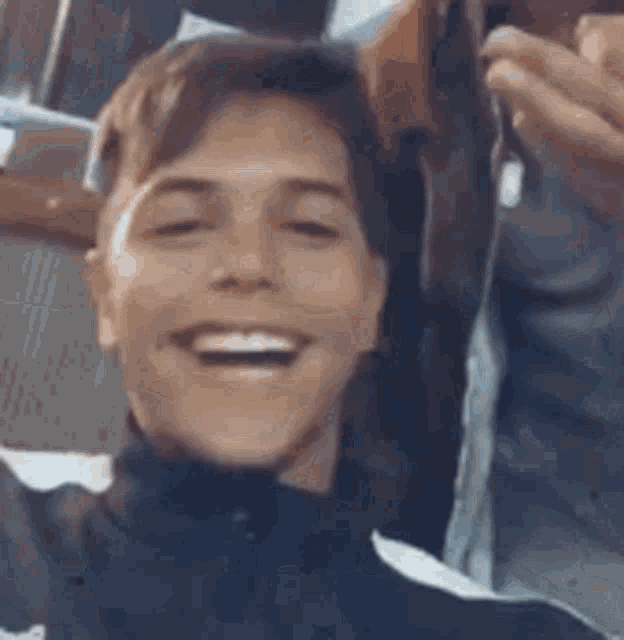 a young man is smiling and looking at the camera while holding a cell phone .