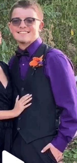 a young man wearing a purple shirt and black vest is standing next to a woman .