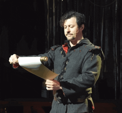 a man in a medieval outfit is holding a scroll of paper