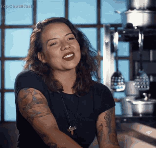 a woman with a tattoo on her arm is smiling in front of a sign that says topchefbrasil