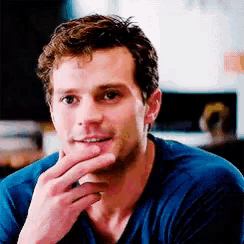 a man in a blue shirt is sitting down with his hand on his chin .