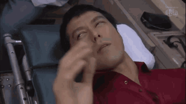 a man in a red shirt is laying in an ambulance with his eyes closed and his hand on his forehead .