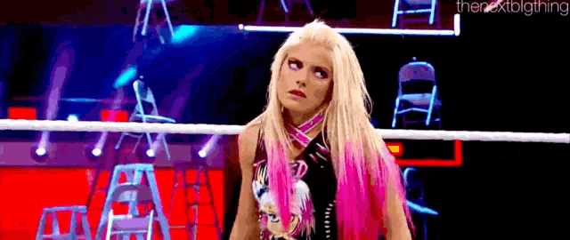 a woman with pink hair is standing in a wrestling ring and looking up .