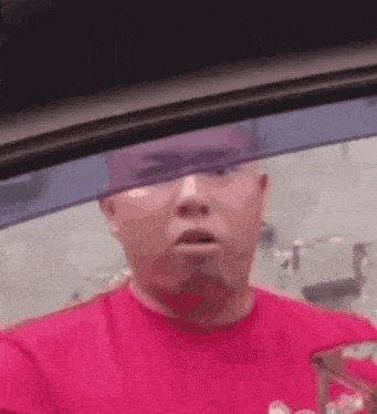 a man in a red shirt is sitting in a car looking out the window .