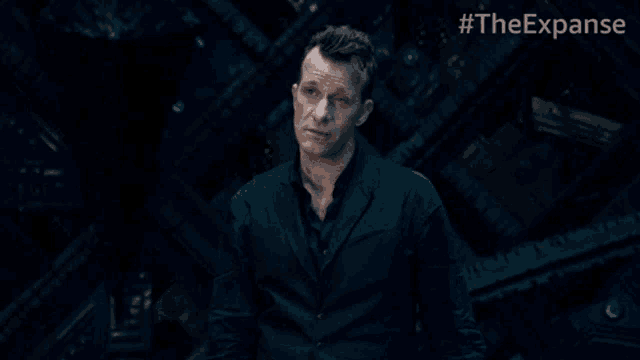 a man in a suit is standing in a dark room with #theexpanse written on the bottom right