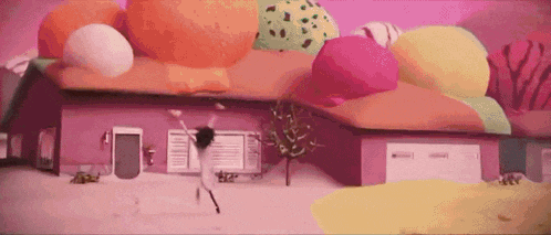 a cartoon character is dancing in front of a pink house covered in ice cream balls .