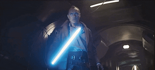 a man is holding a light saber in a dark hallway .