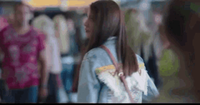 a woman wearing a denim jacket and a backpack with angel wings is standing in a crowded area .