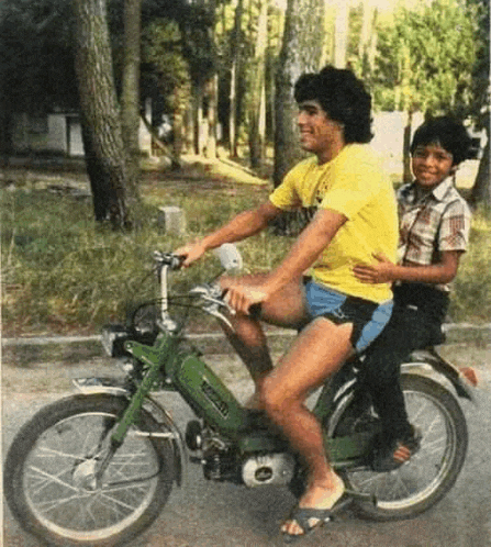 a man in a yellow shirt is riding a motorcycle with a boy on the back .