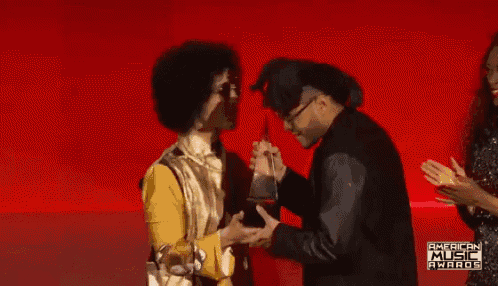 two men are standing in front of a red wall that says american music awards on it