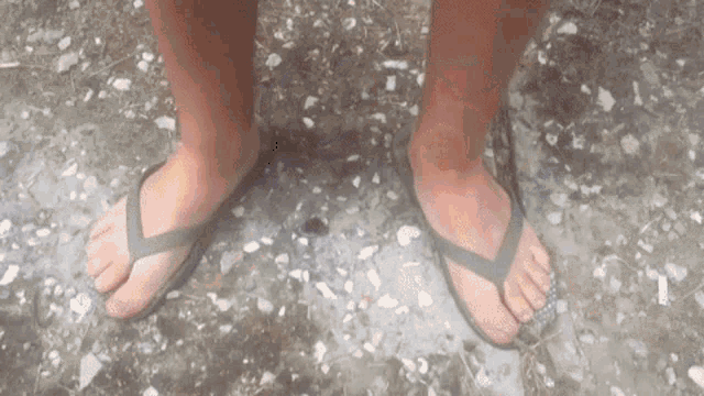 a person wearing flip flops is standing on a gravel ground