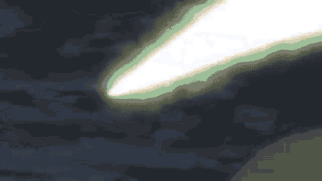 a white light beam is coming out of the sky in a dark cloudy sky .
