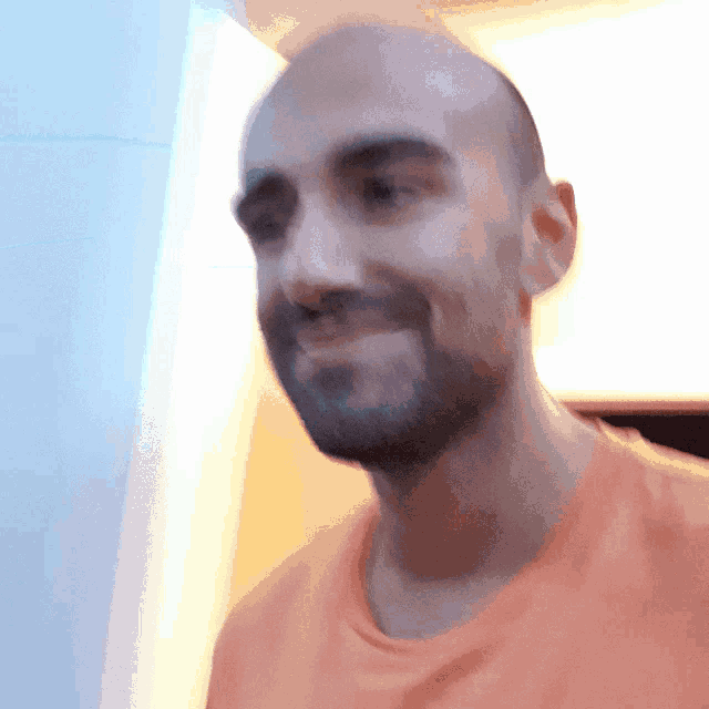 a man with a beard wearing an orange shirt is smiling