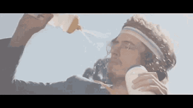 a man is drinking water from a bottle while wearing a headband .