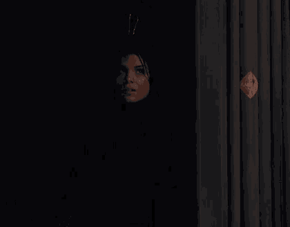 a woman is standing in the dark behind a curtain .